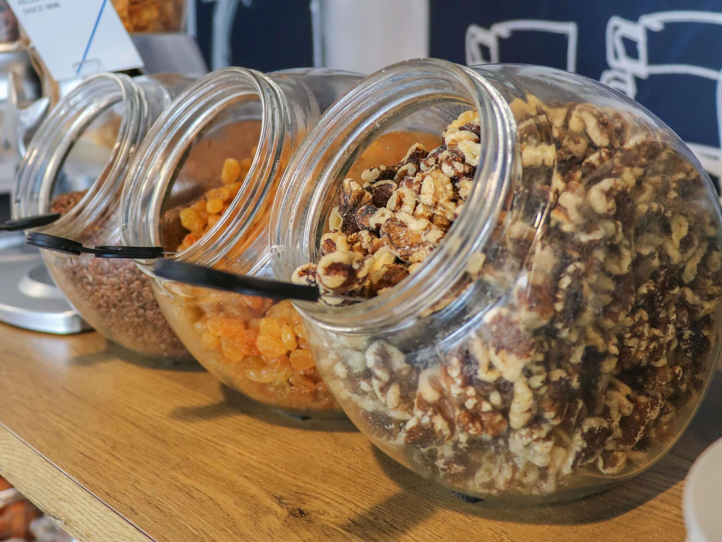 A row of glass jars filled with various granola and nuts on a wooden surface.