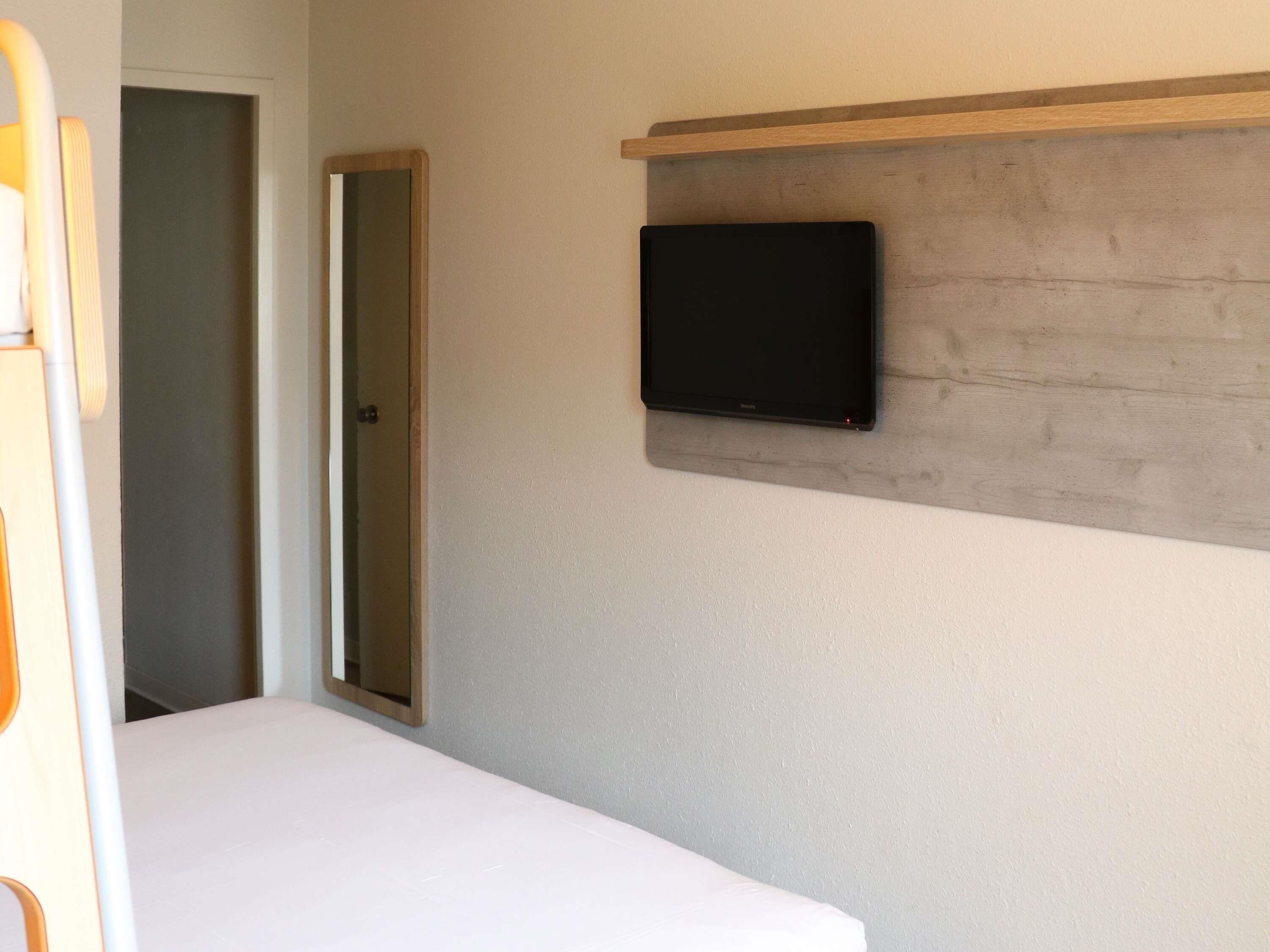 A bedroom with a bed, a television mounted on a wooden shelf, and a door leading to another room.