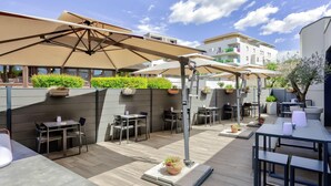 Un área de patio al aire libre con mesas, sillas, sombrillas y plantas en macetas.