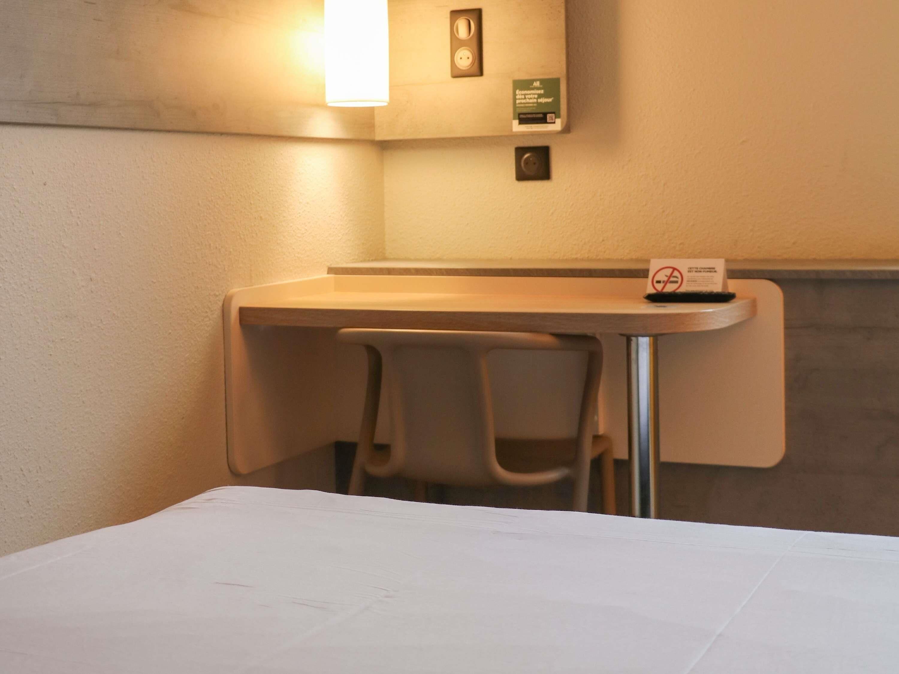 Um espaço de trabalho pequeno e reservado, com escrivaninha, duas cadeiras e uma cama.
