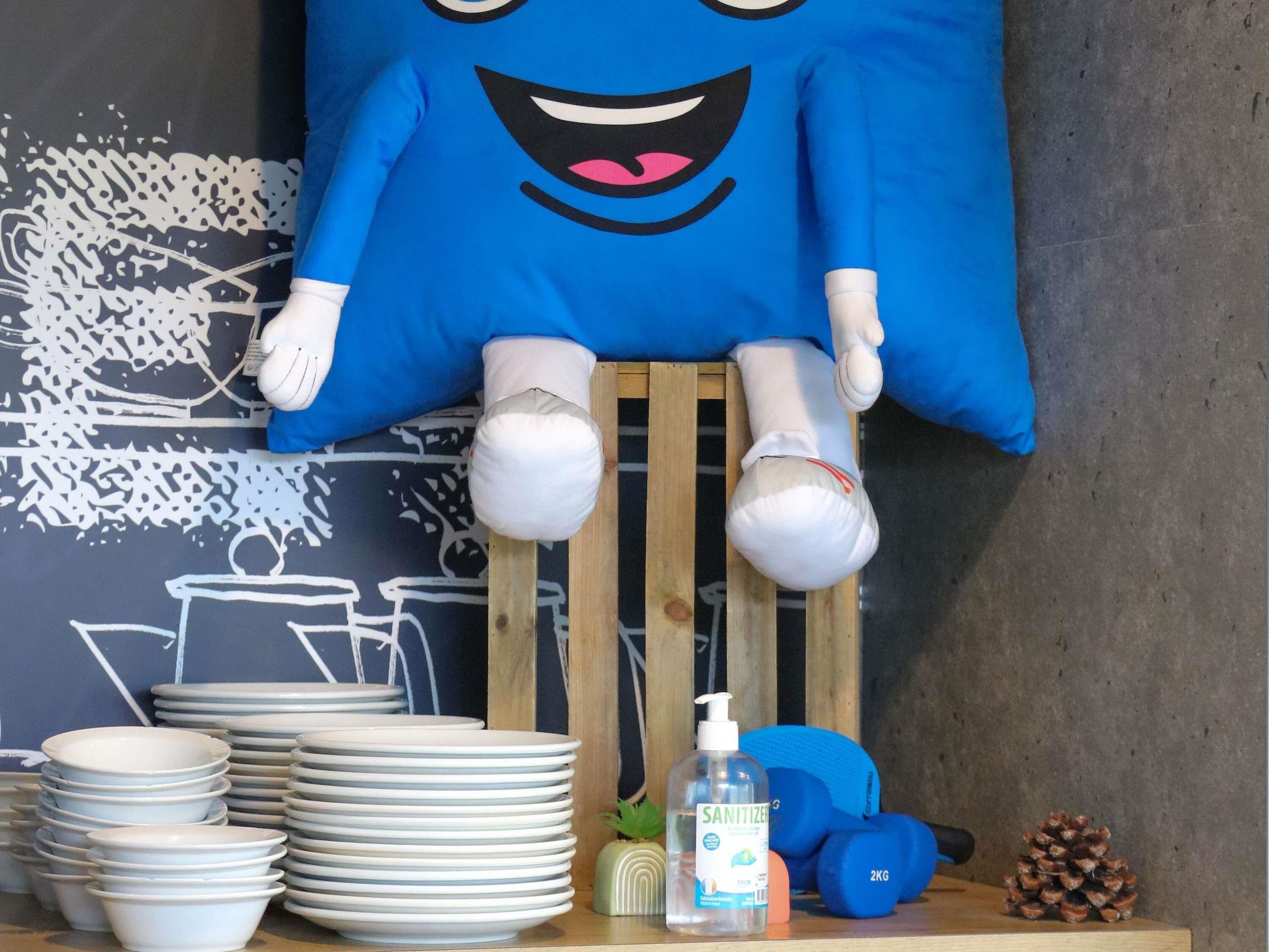 Una stanza con un peluche azzurro, ciotole bianche impilate, una bottiglia di disinfettante, manubri azzurri e un pigna.