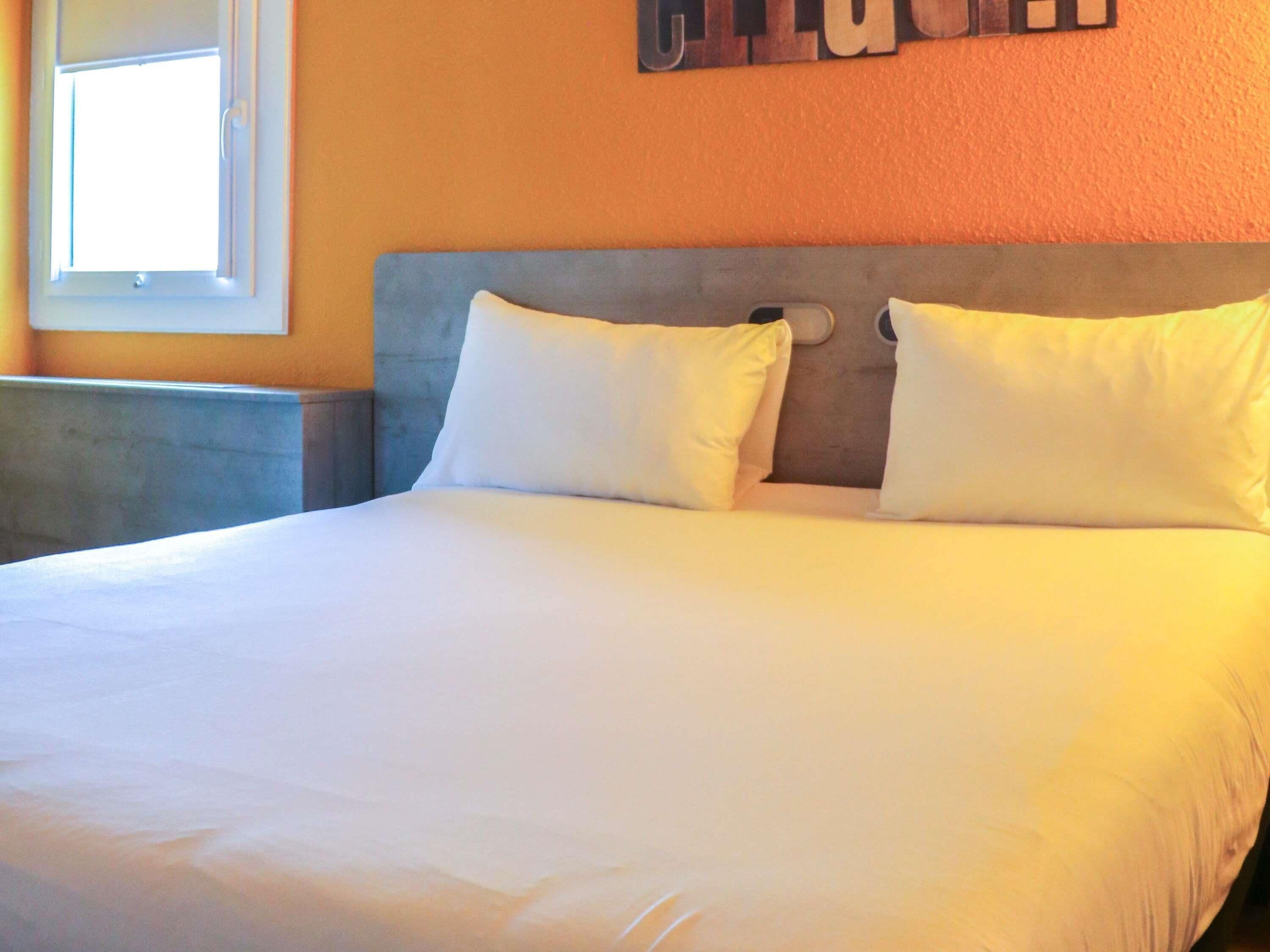 A bed with white bedding, a grey headboard, and two pillows.