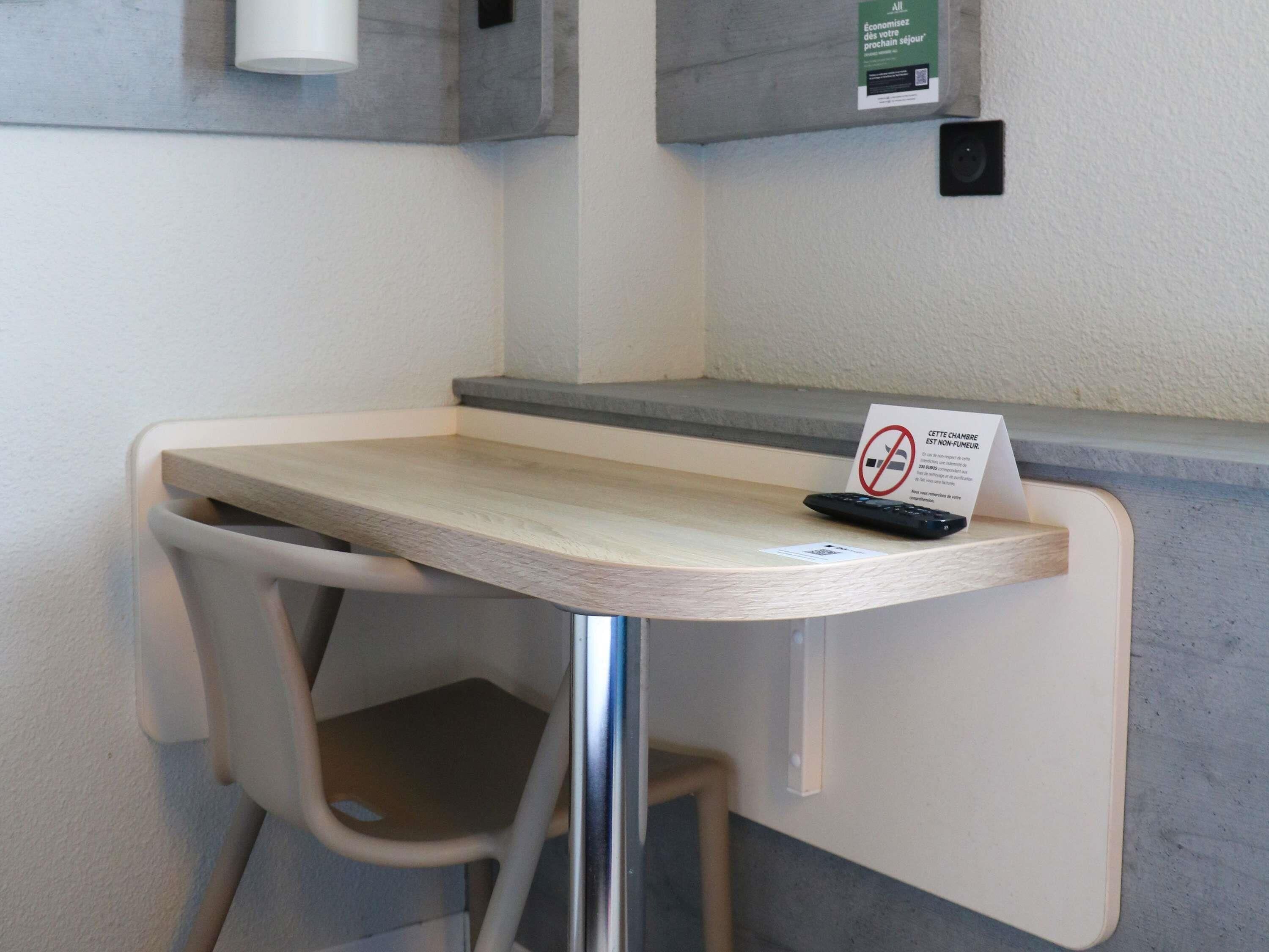 Ein kleiner Tisch mit einem Rauchverbotsschild, einer Fernbedienung und einem Stuhl.