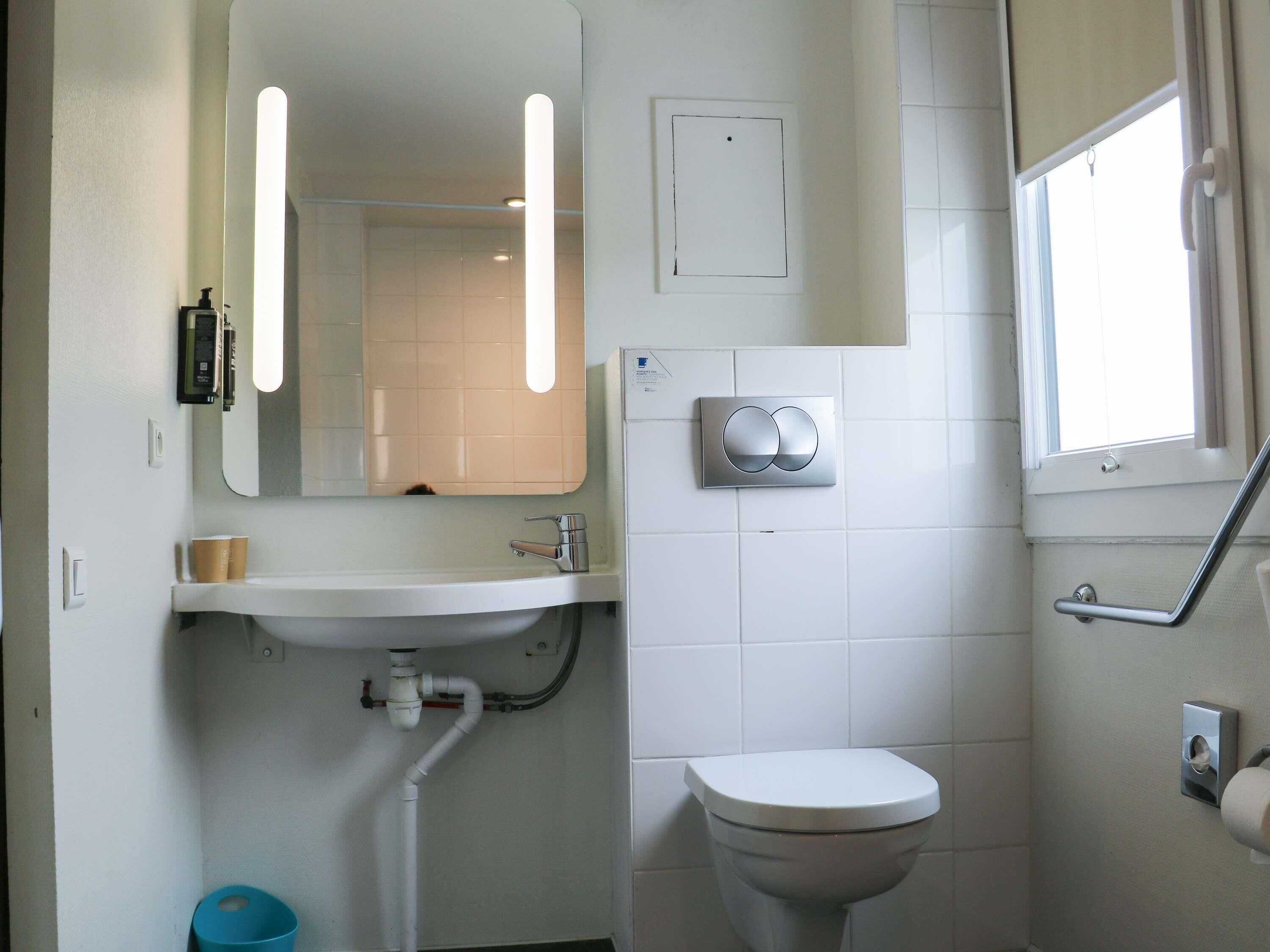Un baño con lavamanos blanco, espejo, inodoro y ventana.
