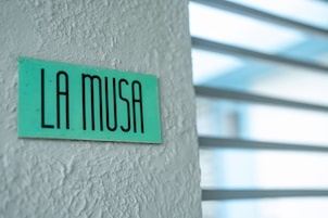 Una señal con el texto "LA MUSA" en una pared con textura.
