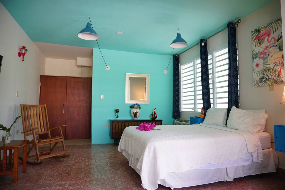 A bedroom with a bed, a wooden chair, a dresser, and a window with curtains.
