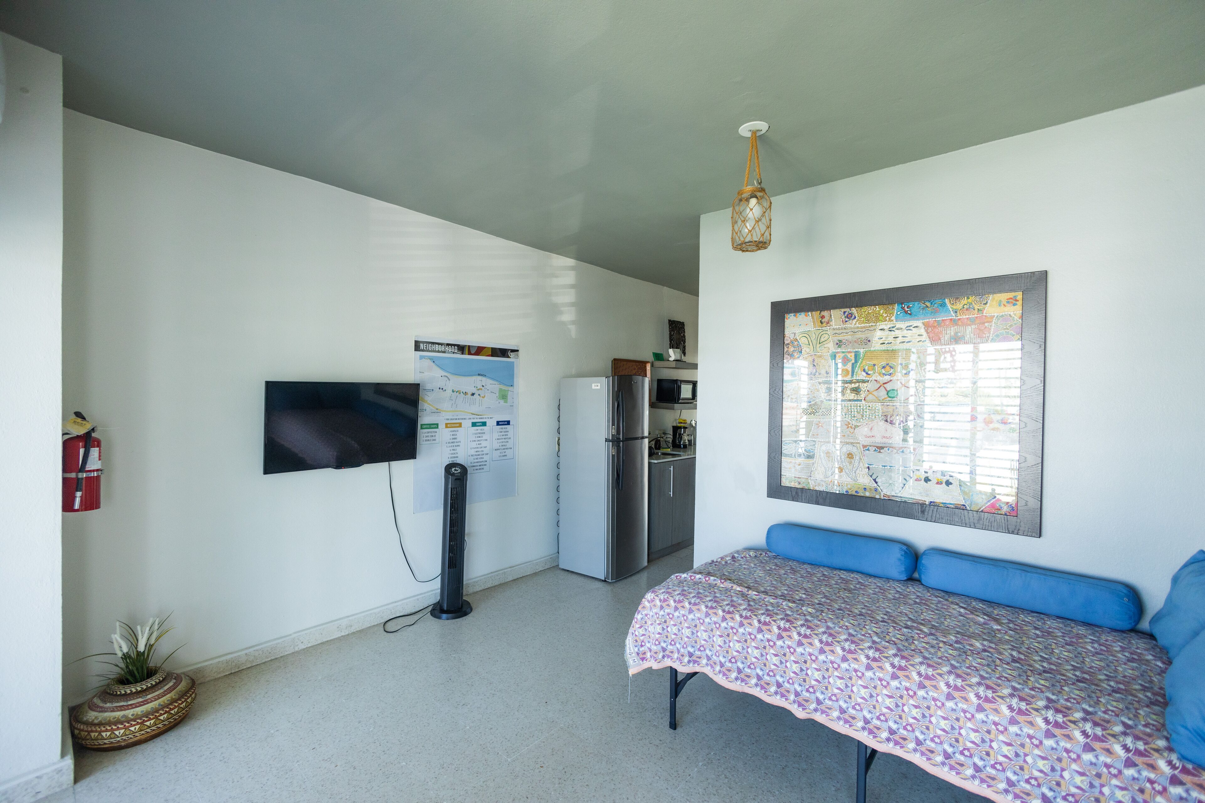 Una habitación pequeña y bien iluminada con una cama, un televisor de pantalla plana, un refrigerador y un mapa colgado en la pared.