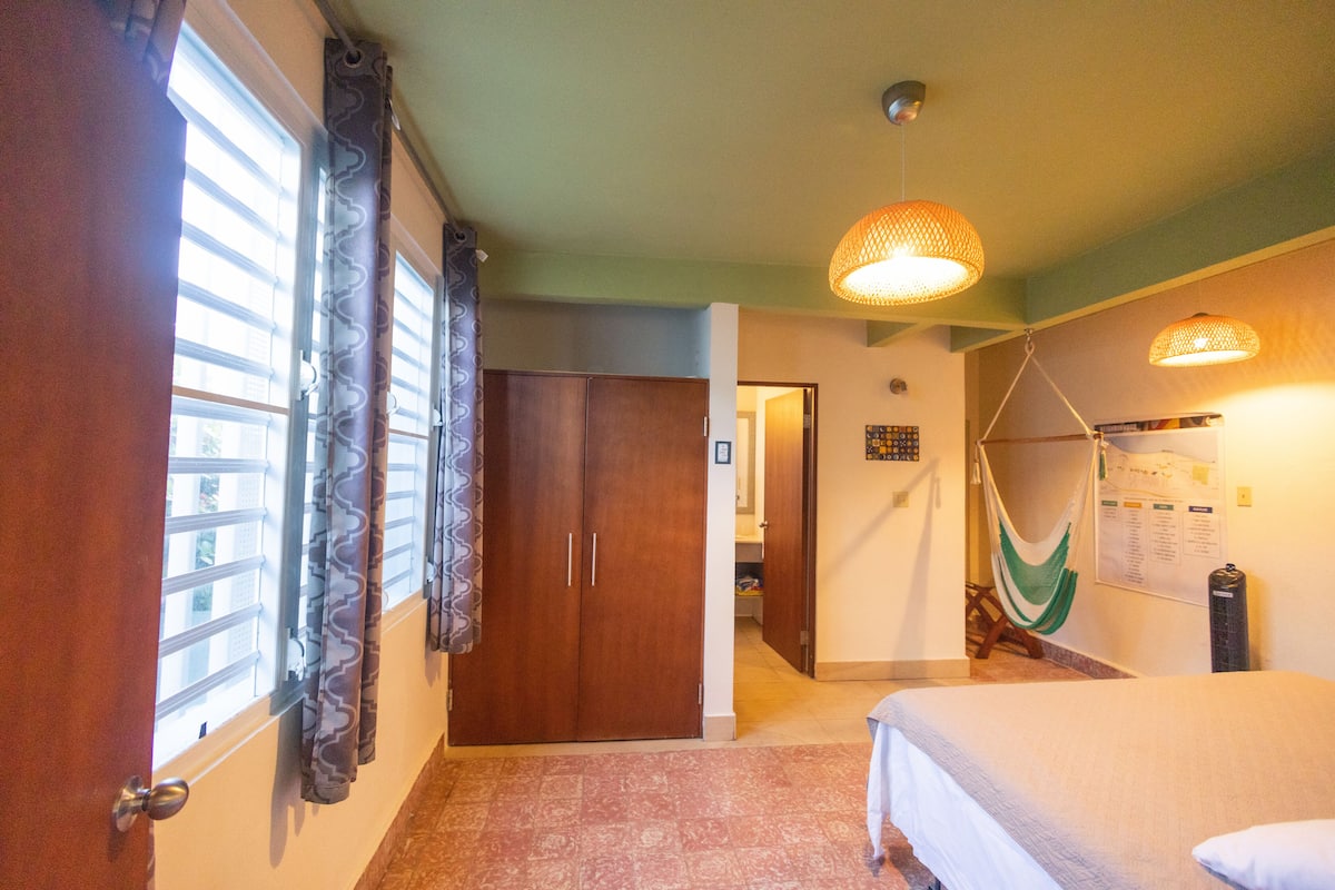 A bedroom with a bed, a wardrobe, a hammock, and a window with curtains.