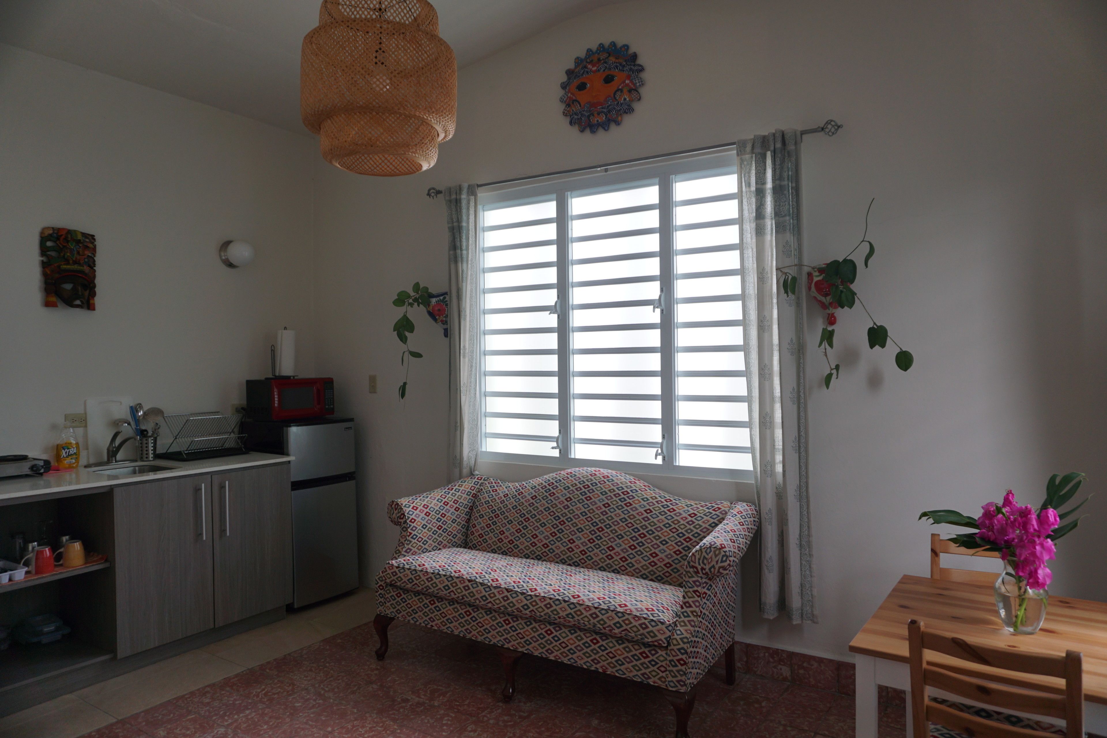 A compact living space with a kitchenette, a sofa, a dining table, and a large window with curtains.