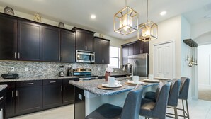 A modern kitchen with dark cabinets, granite countertops, stainless steel appliances, and a central island with bar stools. - Solterra - 5431 Solterra Circle (Davenport)