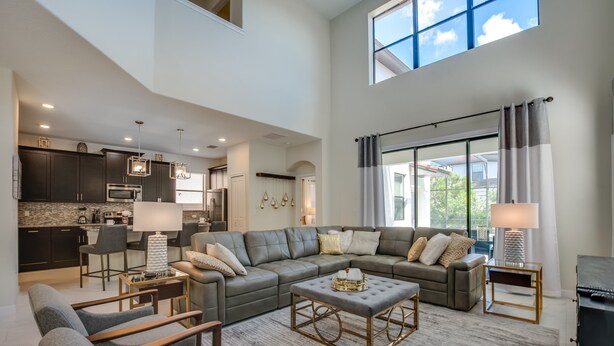 A spacious living area with a grey sectional sofa, a coffee table, and a dining area with a chandelier. - Solterra - 5431 Solterra Circle (Davenport)