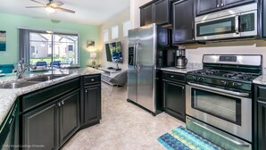 A modern kitchen with dark cabinetry, stainless steel appliances, and a large window overlooking a backyard.
