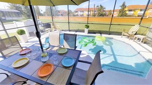 An outdoor patio with a table set for dining, a swimming pool with floating toys, and a view of a residential area. - Bella Vida - 470 Las Fuentes Dr (Kissimmee)