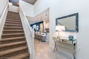 A staircase leading to a kitchen area with bar stools and a glass-top console table. - Windsor at Westside - 1816 Gobi Drive (Kissimmee)
