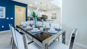 A modern dining area with a dark wooden table set for six, white chairs, and a vase with white flowers.