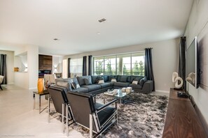 A modern living room with a sectional sofa, a glass coffee table, and a large window with curtains. - Solara Resort - 9043 Sunshine Ridge Loop (Kissimmee)