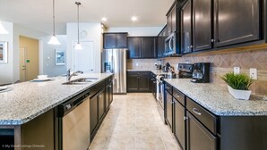 Une cuisine moderne avec des meubles de couleur sombre, des appareils en acier inoxydable, des plans de travail en granit et des luminaires suspendus.