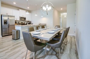 Cozinha moderna com eletrodomésticos de aço inoxidável, uma ilha central com assentos e uma área de jantar preparada para seis pessoas.