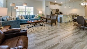 Un salon spacieux avec un canapé bleu, un divan en cuir marron et un coin repas comprenant une table et des chaises.