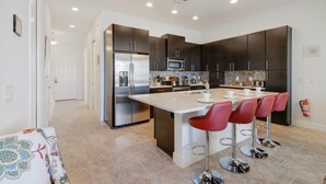A modern kitchen with dark cabinets, stainless steel appliances, a central island with bar stools, and a tiled backsplash. - Festival Resort - 349 Captiva Dr (Davenport)