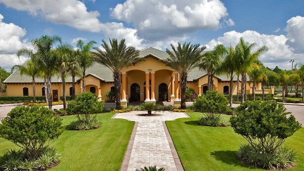 A yellow building with a central courtyard, surrounded by palm trees and well-maintained lawns.