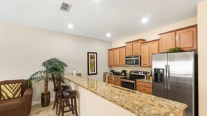 A modern kitchen with granite countertops, stainless steel appliances, wooden cabinets, and a bar stool area.