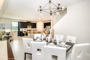 Un espace de salle à manger moderne avec une table noire dressée pour quatre personnes, des chaises blanches et un lustre original.