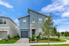A modern two-story townhouse with a stone accent wall, a front garage, and well-maintained landscaping.