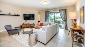 A modern living room with a sofa, armchair, and a TV mounted on the wall. - Solterra - 4175 Oaktree Drive (Davenport)