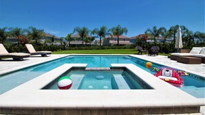 A swimming pool with lounge chairs, a hot tub, and a view of houses in the background.