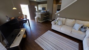 Ein Wohnzimmer mit Klavier, einer Couch und einer Küche im Hintergrund.