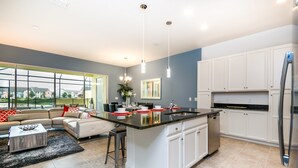 Une cuisine moderne avec des meubles blancs, un grand îlot central et un coin repas comprenant un canapé et une table basse.