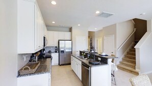 A modern kitchen with white cabinets, a stainless steel refrigerator, granite countertops, and a built-in dishwasher.
