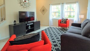 A living room with a TV, red and gray sofas, a patterned rug, and a window with curtains. - Terra Verde Resort - 101 Pompano Beach Dr (Kissimmee)