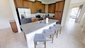 A kitchen with granite countertops, stainless steel appliances, wooden cabinets, and bar stools.
