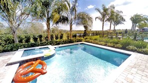 En swimmingpool med et boblebad, omgivet af frodig vegetation og palmer.