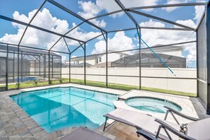 Une piscine avec un jacuzzi, entourée d’un patio couvert équipé de chaises longues.