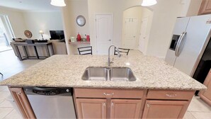 A kitchen with granite countertops, stainless steel sink, and wooden cabinets. - Paradise Palms - 8876 Candy Palm Road (Kissimmee)