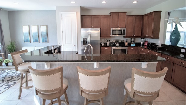A modern kitchen with a central island, bar stools, stainless steel appliances, and wooden cabinets. - Encore Resort at Reunion - 791 Lasso Drive (Kissimmee)