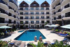 Un hôtel à plusieurs étages doté d’une piscine centrale, entourée de transats et de parasols.