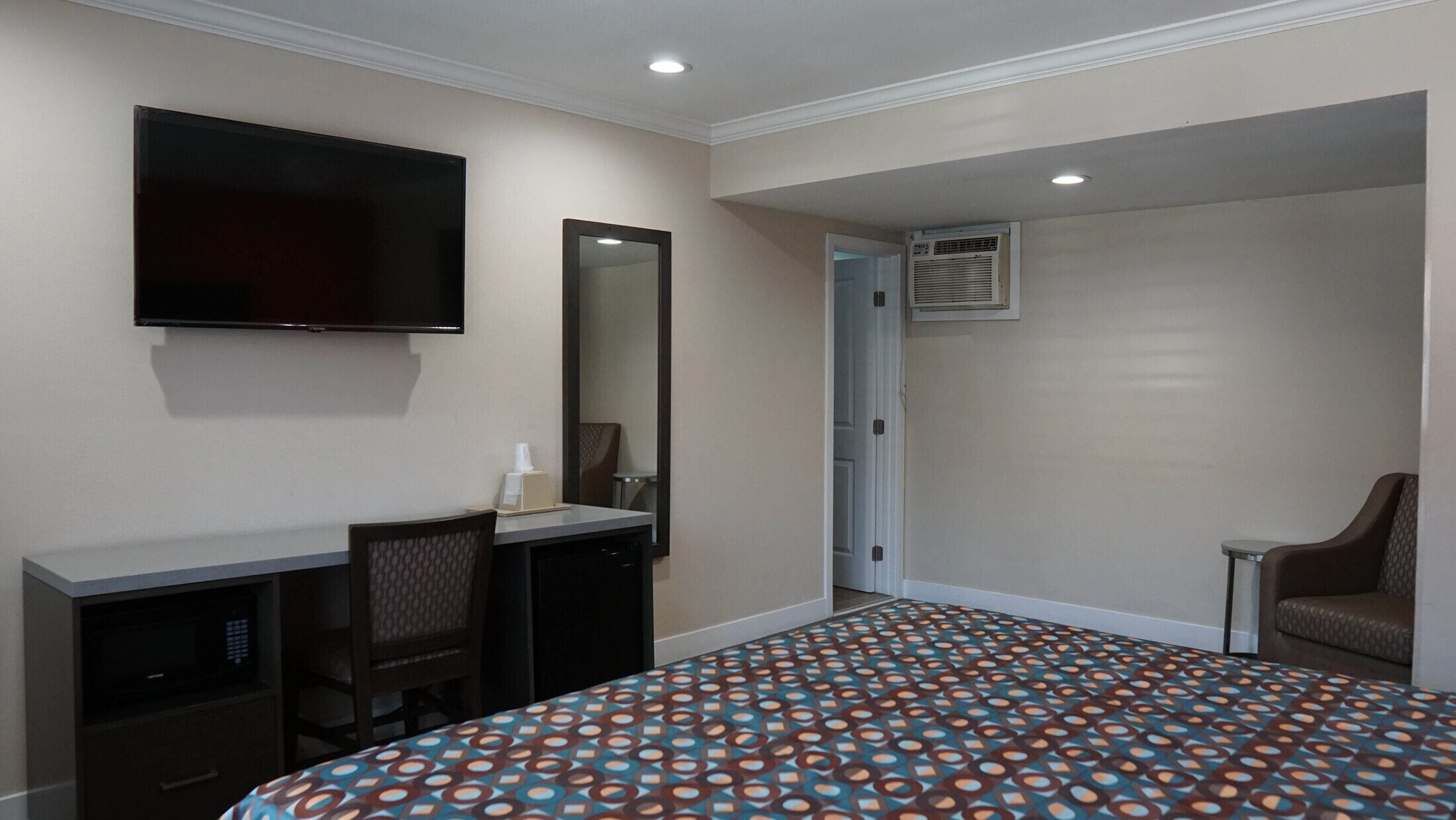 A hotel room with a bed, a desk, a chair, a television, and an air conditioning unit.