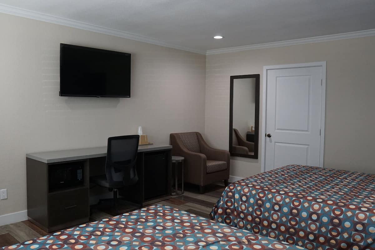 Hotelkamer met een bureau, stoel, twee bedden met beddengoed met een patroon, een televisie, een deur en een spiegel.