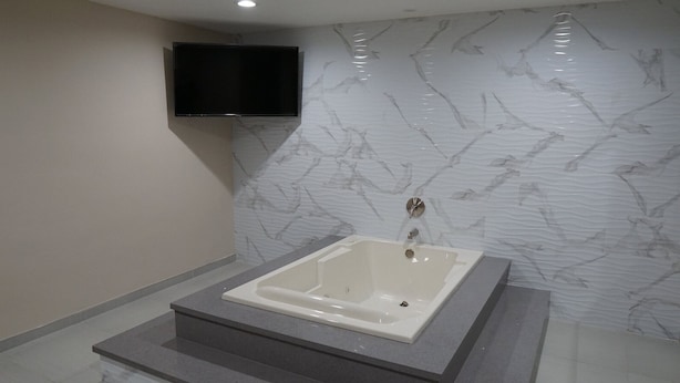Ein modernes Badezimmer mit Marmorwand, einer integrierten Badewanne und einem flachbildschirmfernseher darüber.