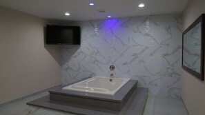 Une salle de bain moderne avec un mur en marbre, un téléviseur encastré et une baignoire sur pied.