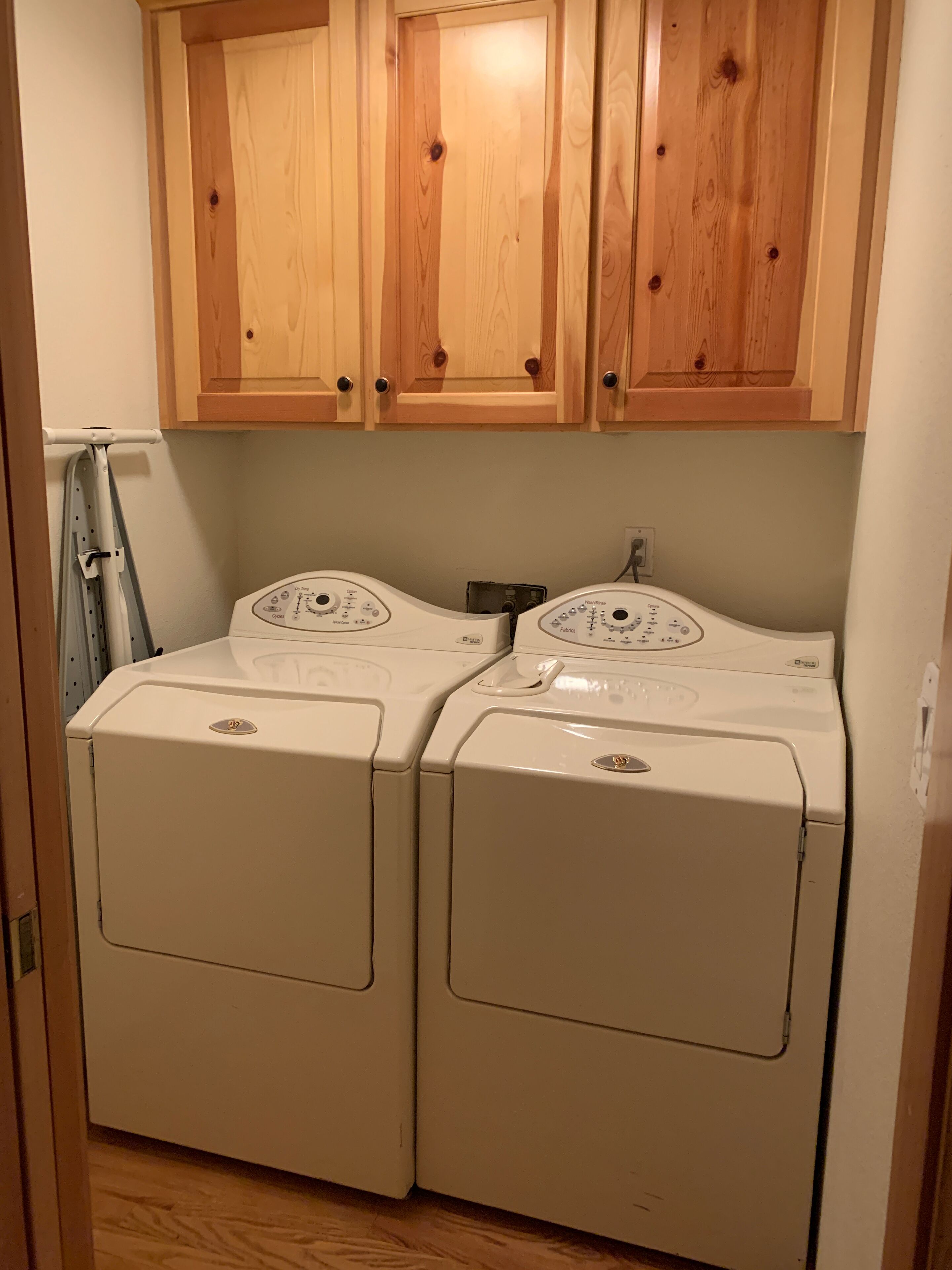 A laundry room with two front-loading washing machines and wooden cabinets above.