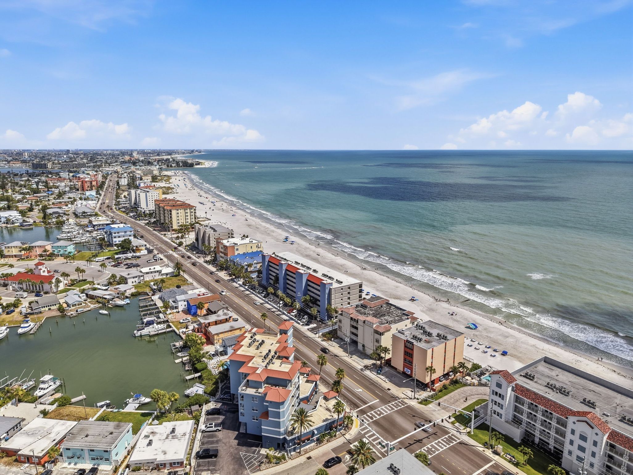 Un paisaje urbano costero con un puerto deportivo, una playa y edificios de varios pisos.