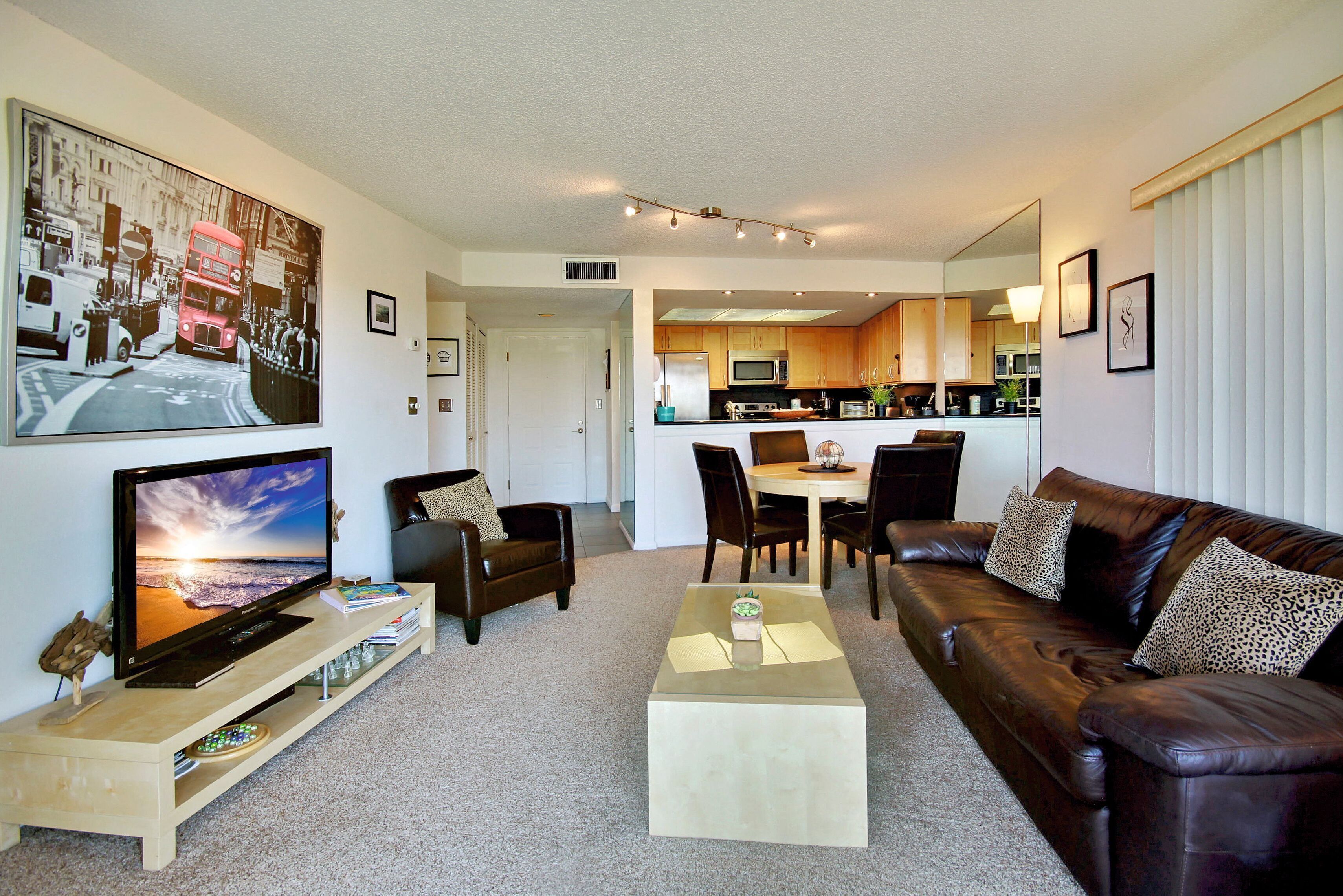 A modern living room with a flat-screen TV, leather sofa, and a dining area with a table and chairs.