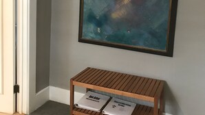 Ein Zimmer mit grauer Wand, einem gerahmten abstrakten Gemälde, einer hölzernen Bank mit zwei Büchern und einer Tür.