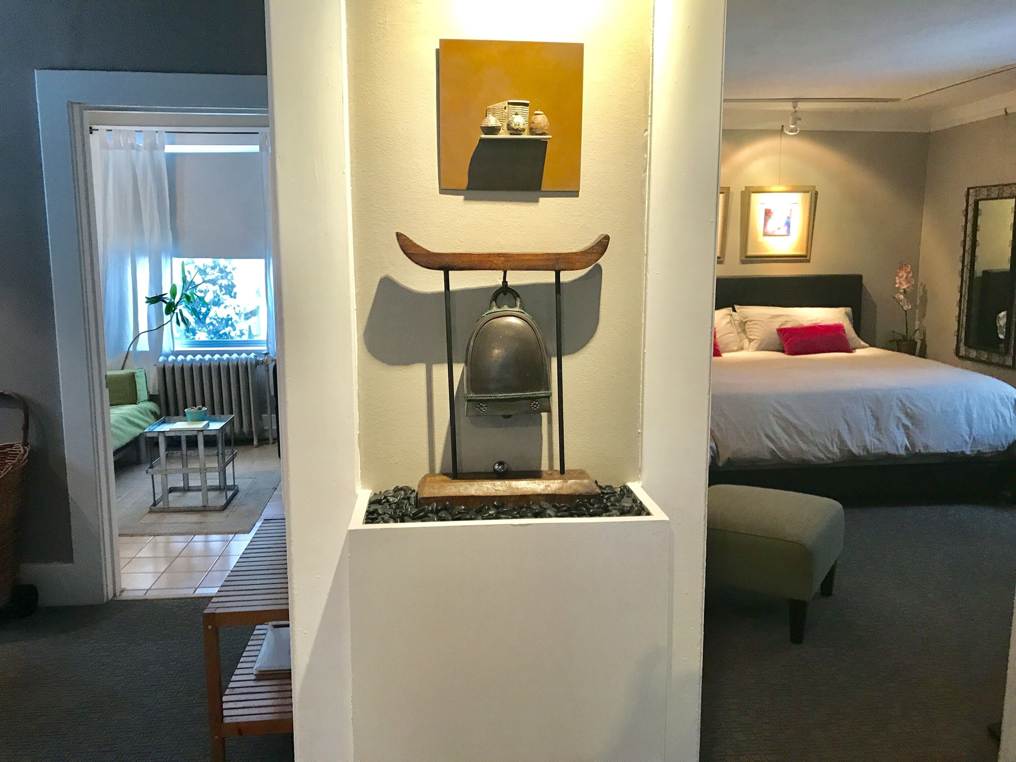 Ein Hotelzimmer mit Bett, Nachttisch, Stuhl, einem kleinen Tisch mit Pflanze und einer Wanddekoration.