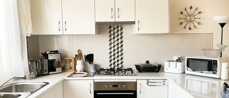 Una cocina moderna con armarios blancos, estufa a gas, horno, microondas y pileta.